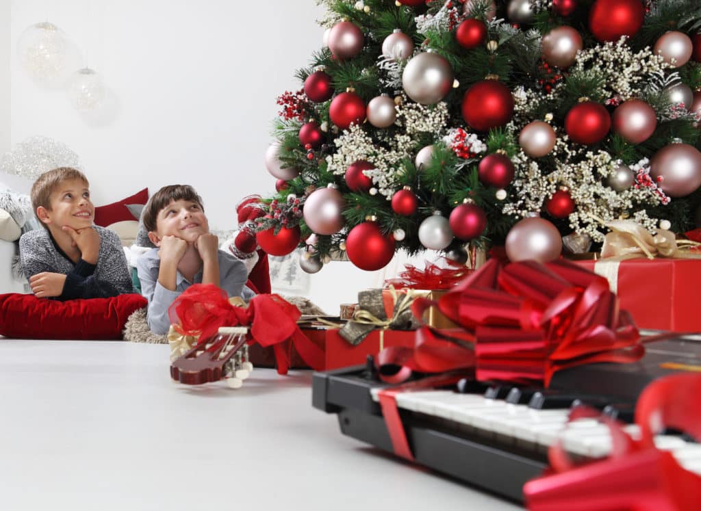 merry christmas and happy holidays, children near the christmas tree with wrapped gift packages and musical instruments, in the living room lying on the floor